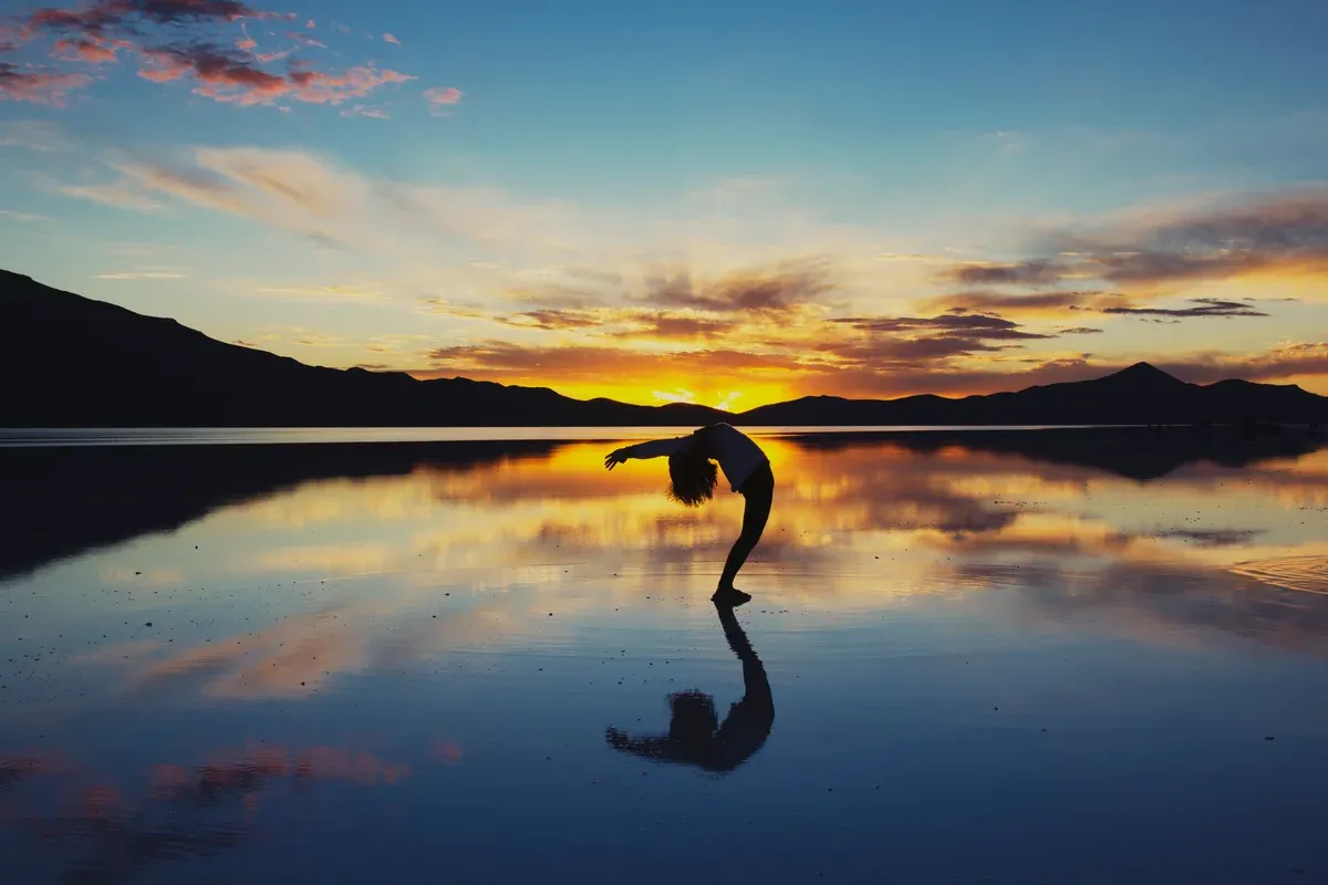 A traveller posing on the mirror at sunset on an Uyuni salt flats tour